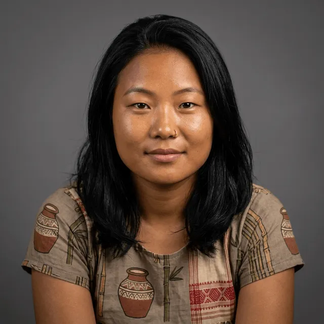 A young woman with long straight black hair and a small gold nose ring, wearing a patterned top, smiling gently at the camera.