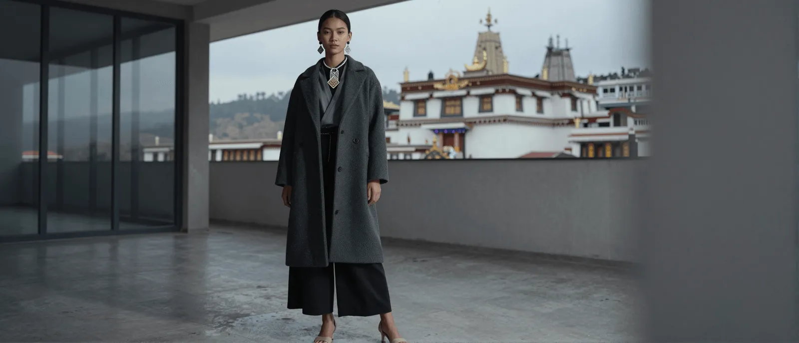 A model in a wool coat and statement jewelry, a Himalayan monastery behind her